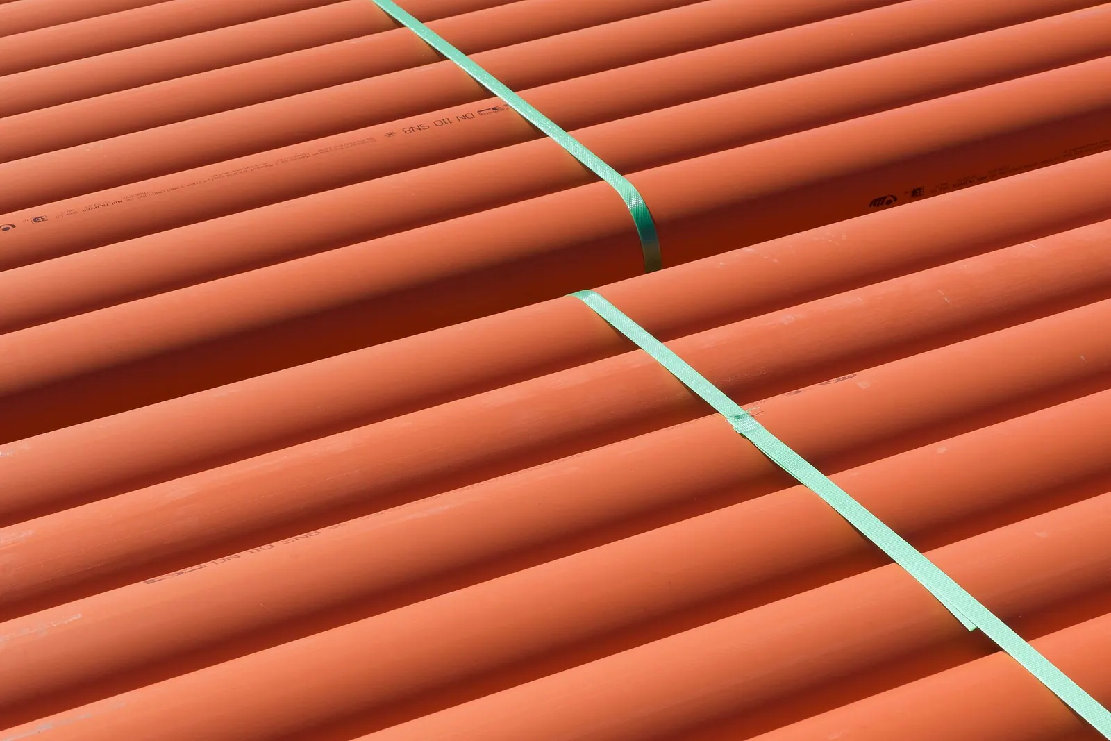 녹색 결속 밴드로 묶어 나란히 쌓아 둔 주황색 PVC 하수관